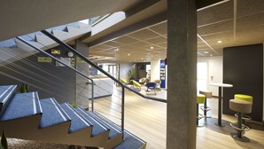 Een modern interieur met een trap naar een lager gelegen niveau, een zithoek met stoelen en een zichtbare vluchtingang.