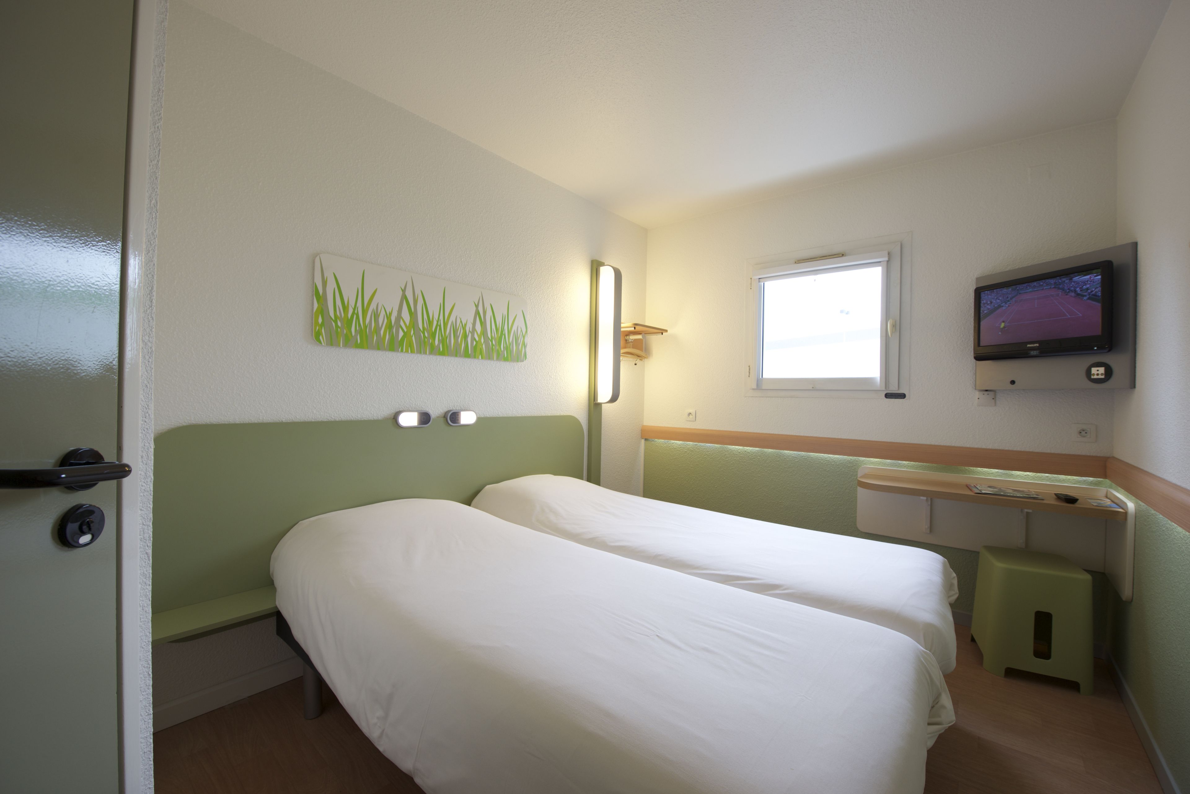 A room with two beds, a window, a television, and a small stool.