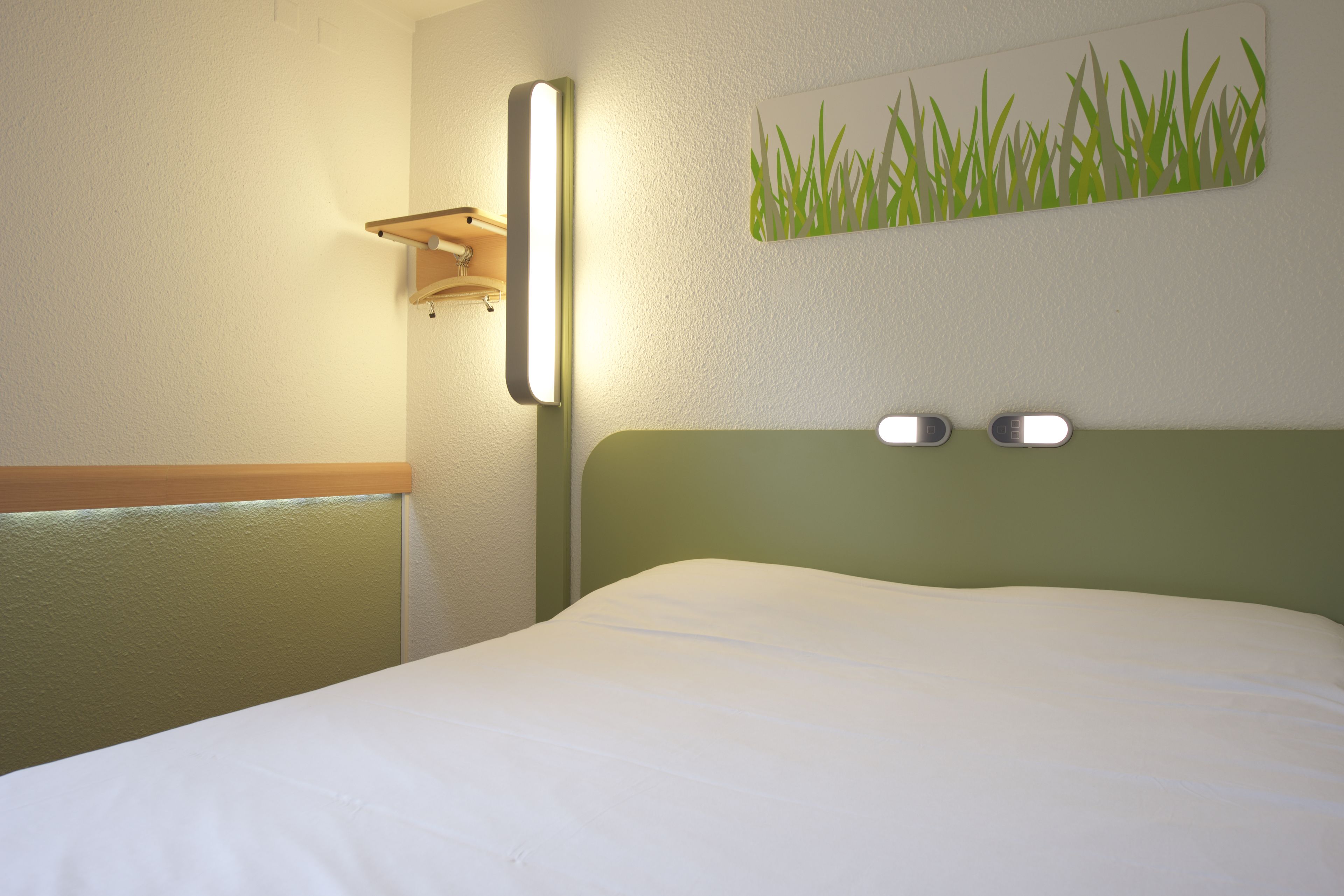 A hotel room with a bed, a wall-mounted light, and a wall art piece.