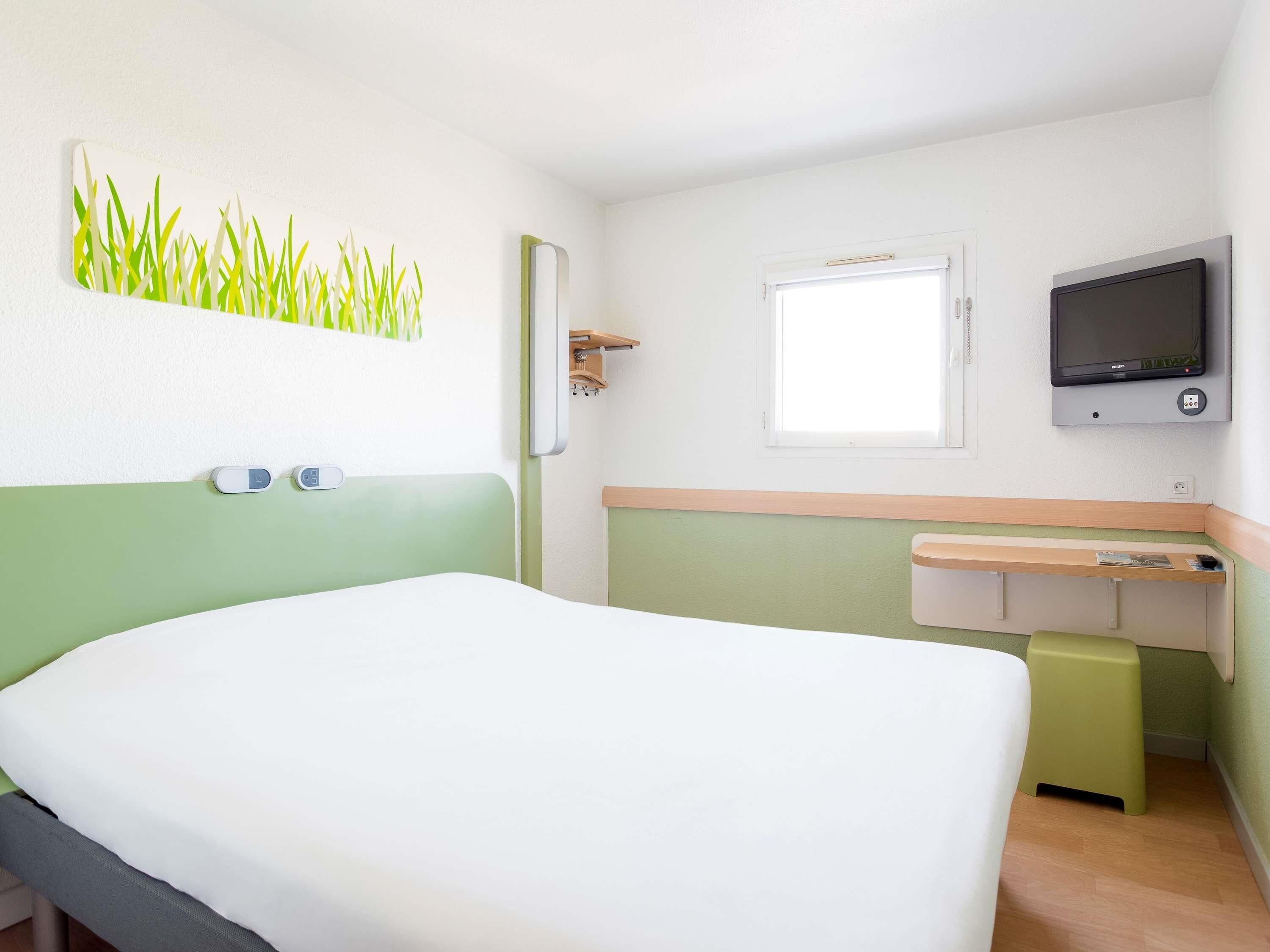 Una habitación de hotel con una cama, un televisor, una ventana y un estante en la pared.