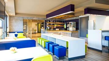 Un restaurante moderno con zona de bar, asientos con taburetes de colores y un mostrador con una variedad de alimentos.