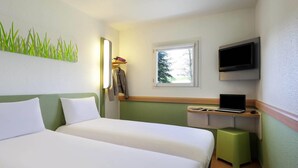 Une chambre d’hôtel avec deux lits, un bureau avec un ordinateur portable, une télévision et une fenêtre donnant sur des arbres.