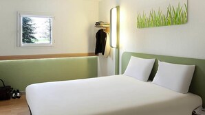 Een hotelkamer met een bed, een raam, een wandlamp en een kunstwerk aan de muur.