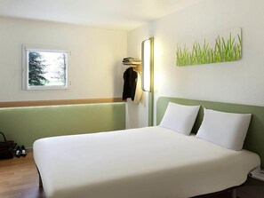 Une chambre d’hôtel avec un lit, une fenêtre, une lampe fixée au mur et une œuvre d’art décorative.