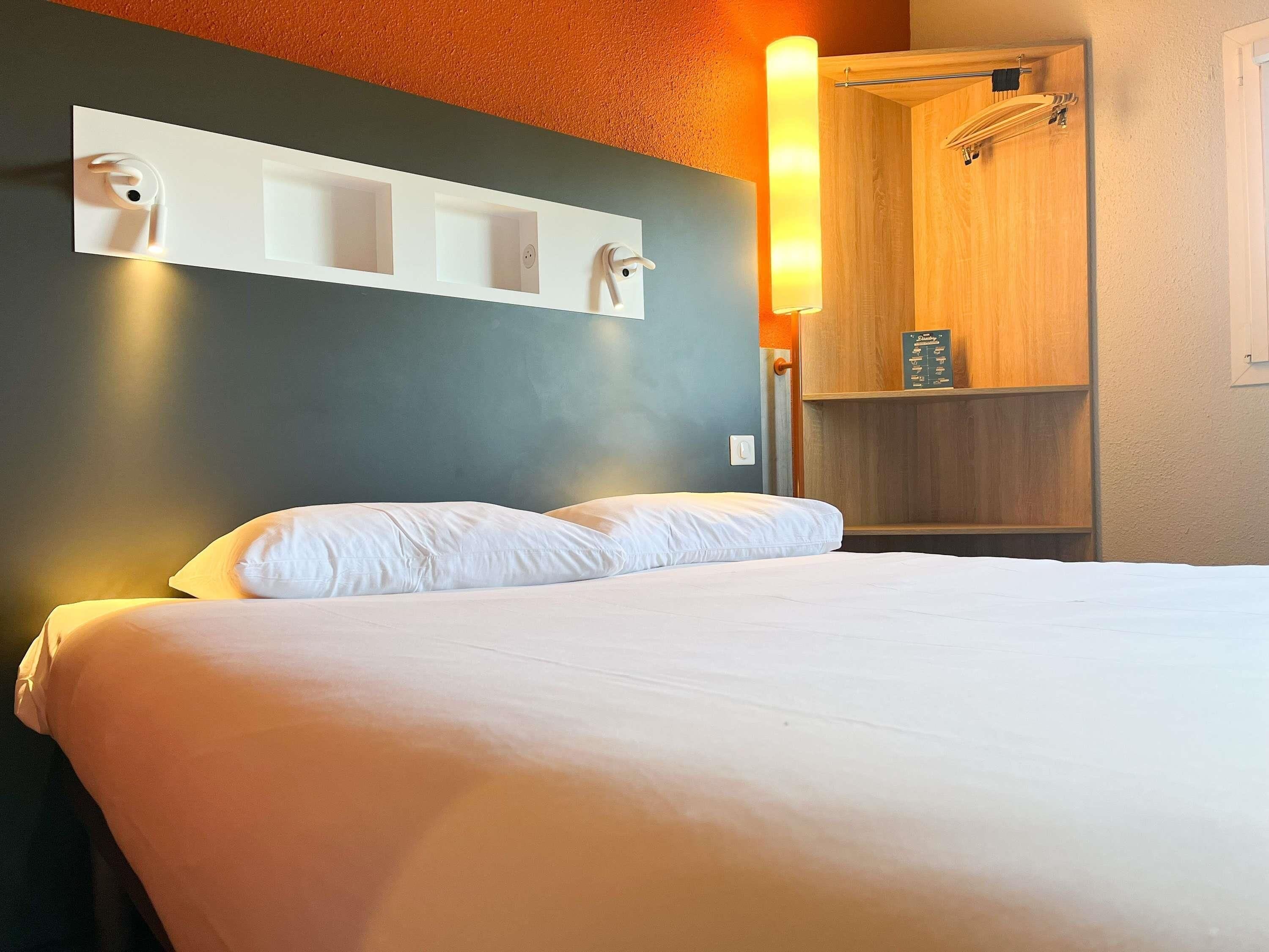 Una habitación de hotel con una cama, un estante con toalla y un armario de madera.