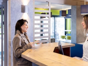 A reception desk with a wooden counter, a modern interior with a mix of natural and industrial elements, and a seating area with a green accent wall. - ibis Budget Carcassonne-La Cité (Carcassonne)