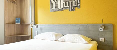 A bed with white bedding, a wooden wardrobe, and a 'Youpi!' sign on the wall.