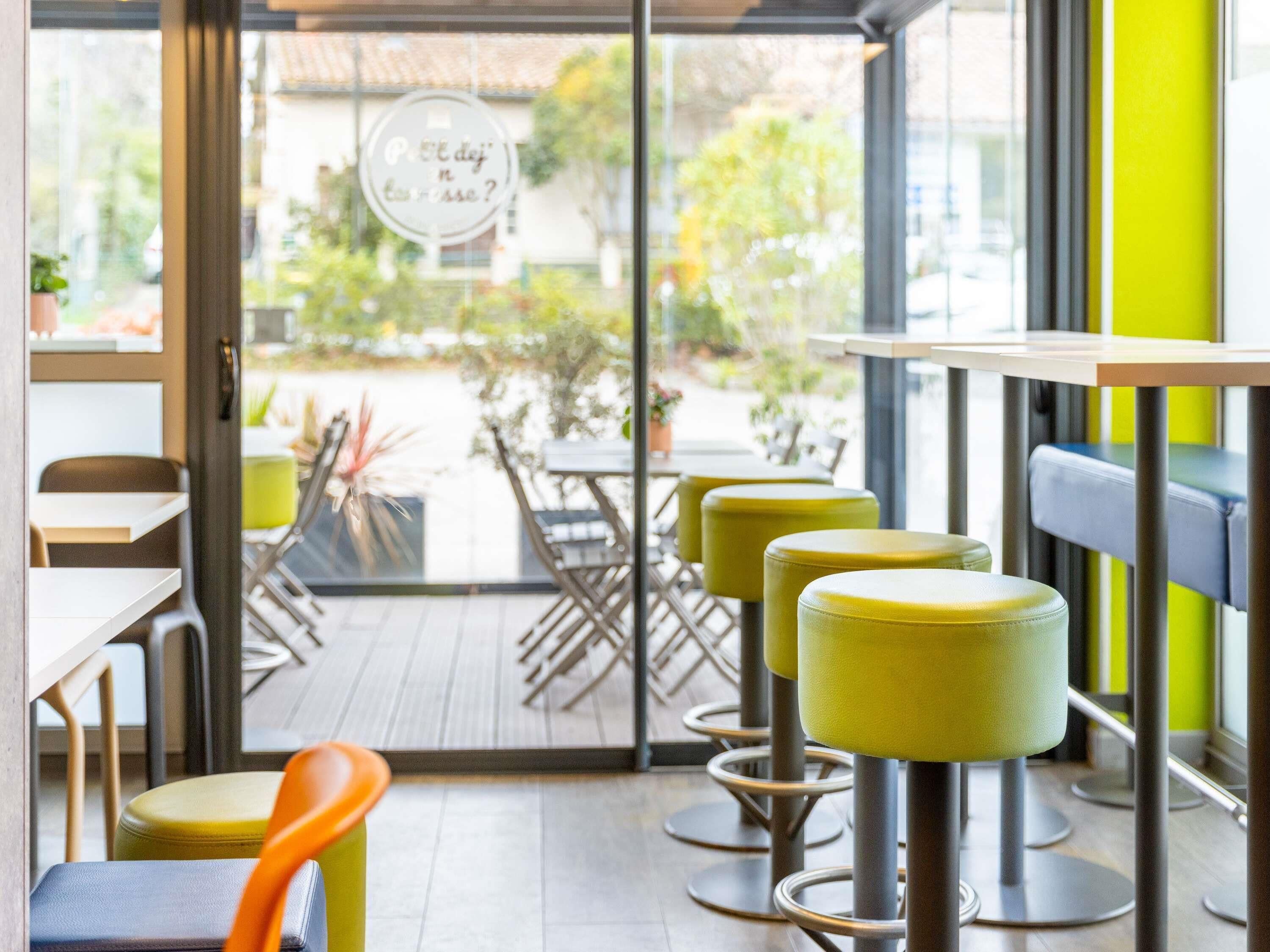 Interior de café com mesas, cadeiras e vista para o exterior.