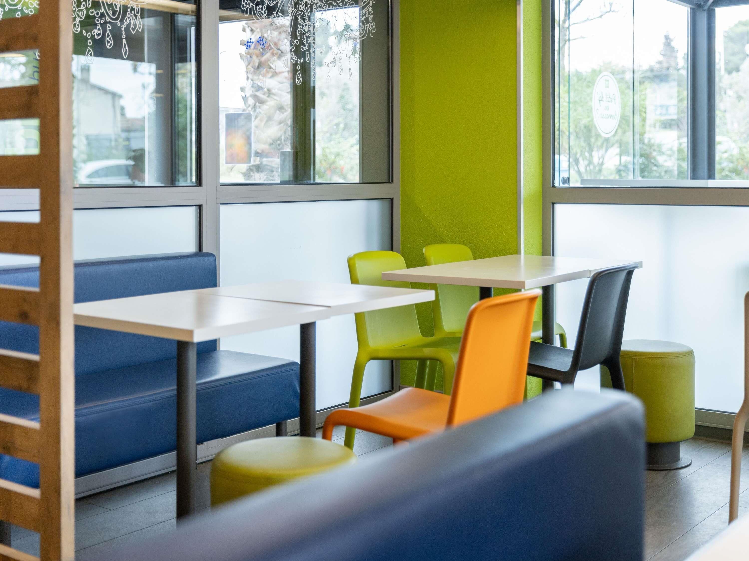 Un comedor moderno con asientos tipo cabina y mesas, ventanas amplias y una pared decorada en color verde.