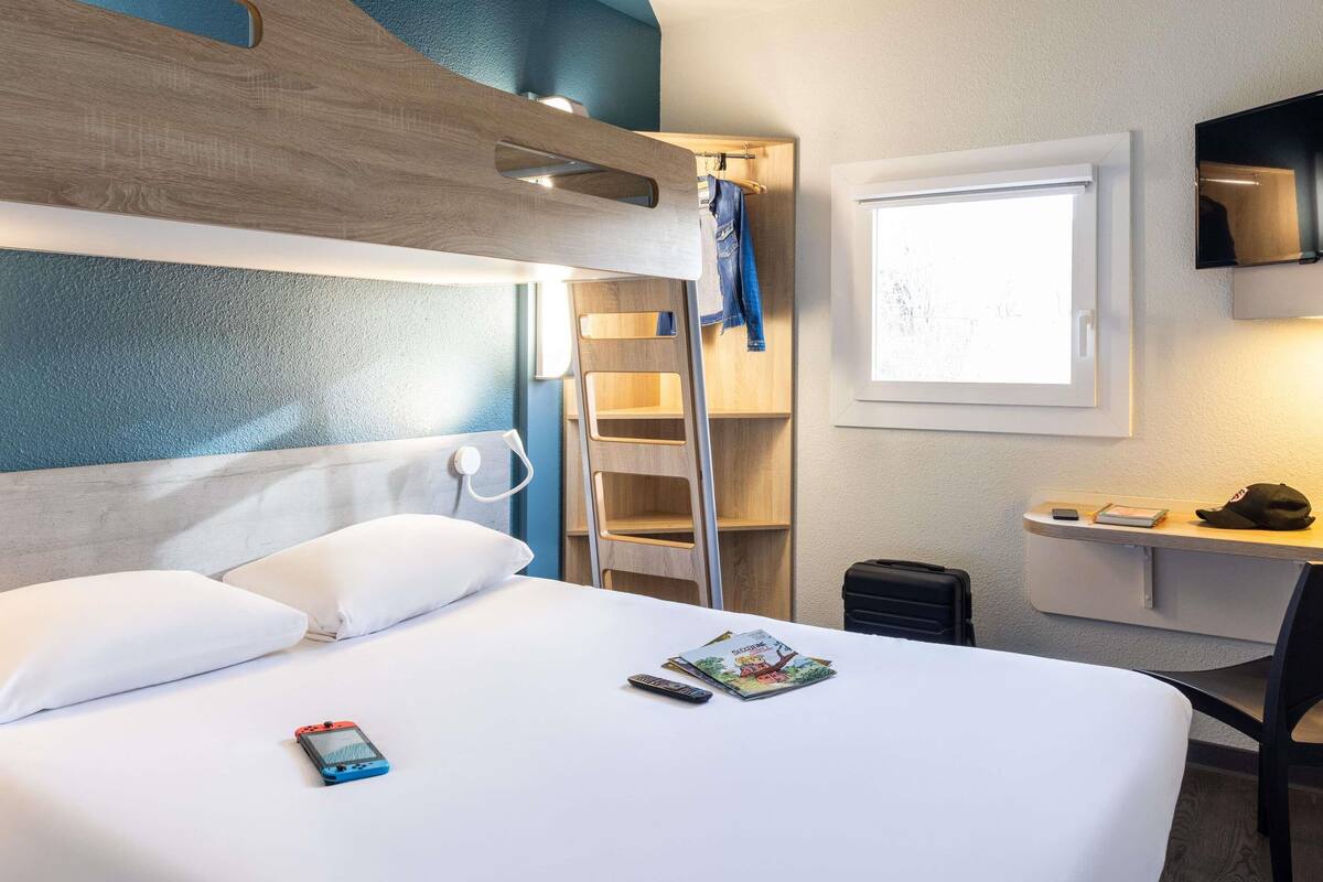 Una habitación de hotel con cama, escritorio, silla, televisión y ventana.