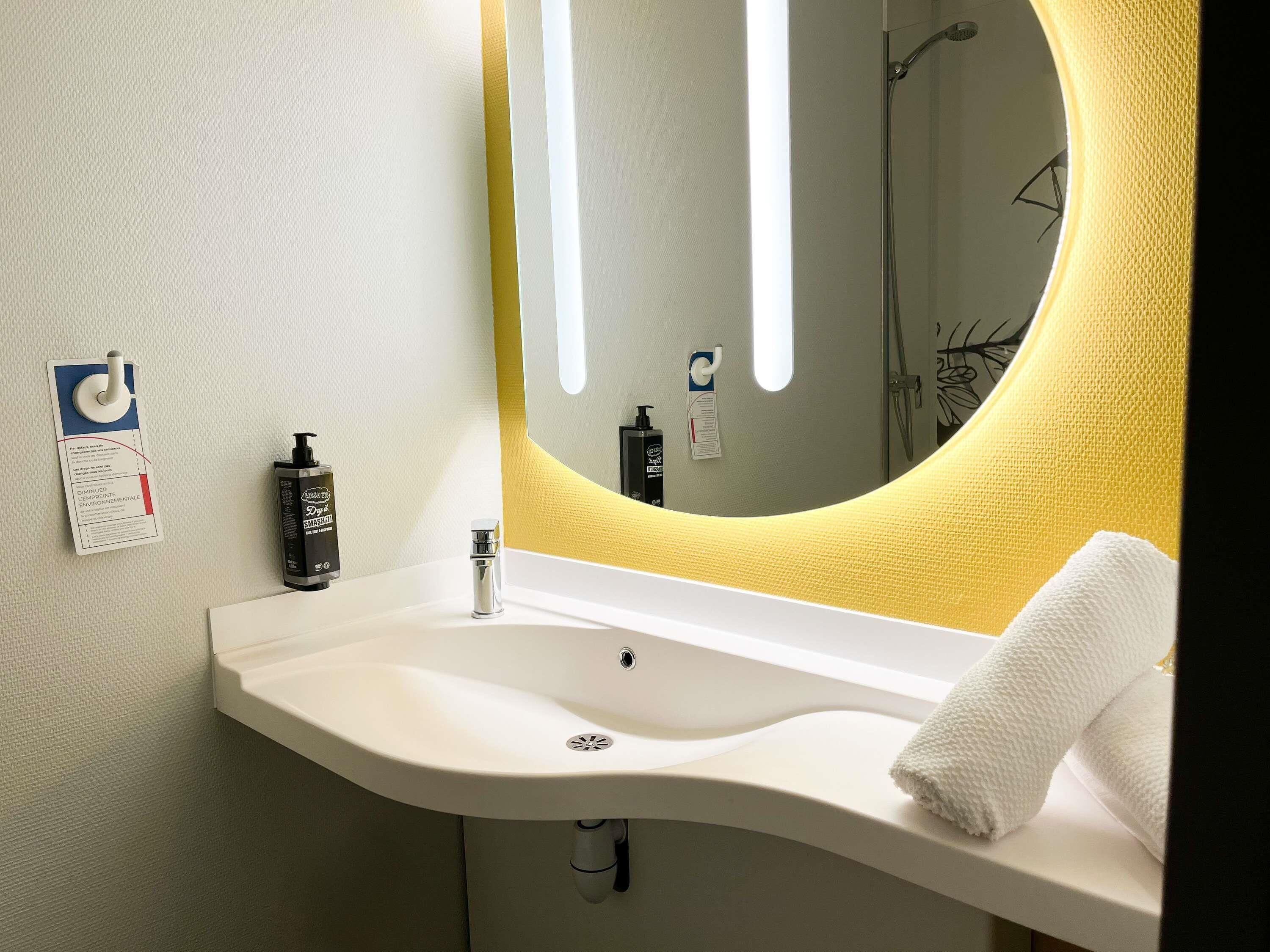 Un baño con un lavamanos blanco, un espejo con un detalle amarillo y una toalla sobre la encimera.