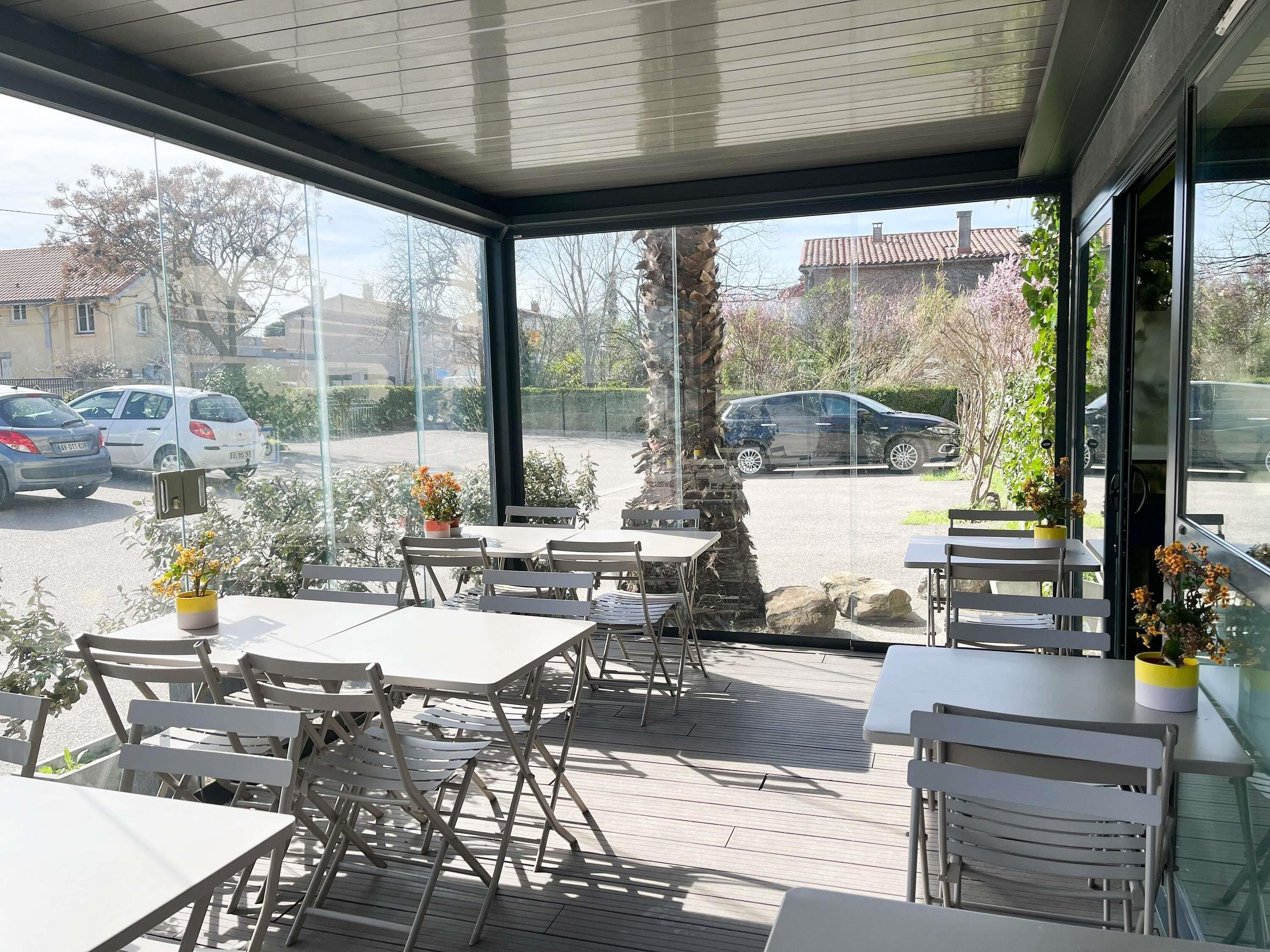 Un patio al aire libre con mesas y sillas, un pilar de piedra y vistas a coches aparcados y edificios.