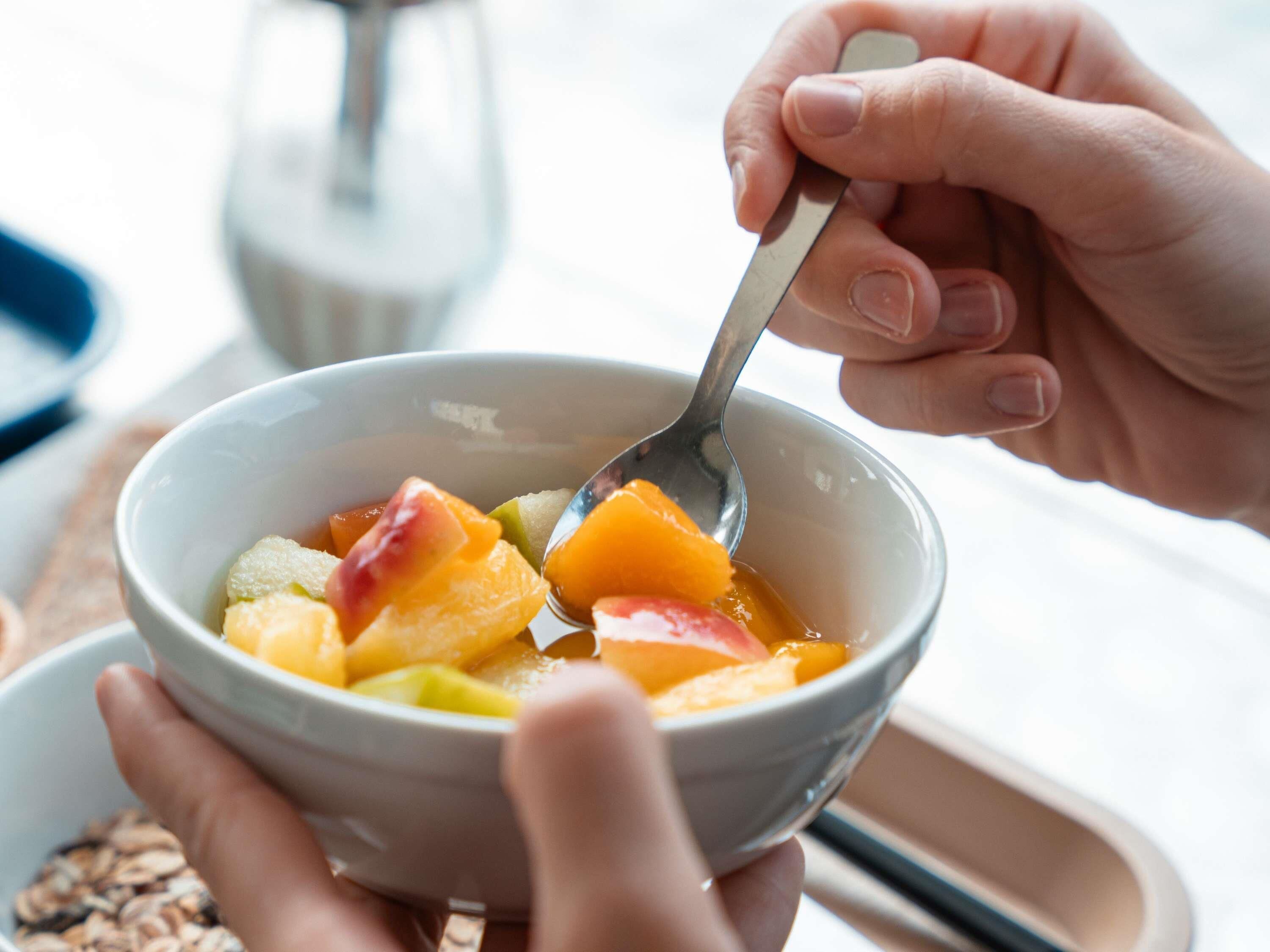 A bowl of fruit with a spoon, held by a person.