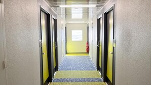 Un couloir d’hôtel avec des portes des deux côtés, une moquette à motifs et une fenêtre au bout.