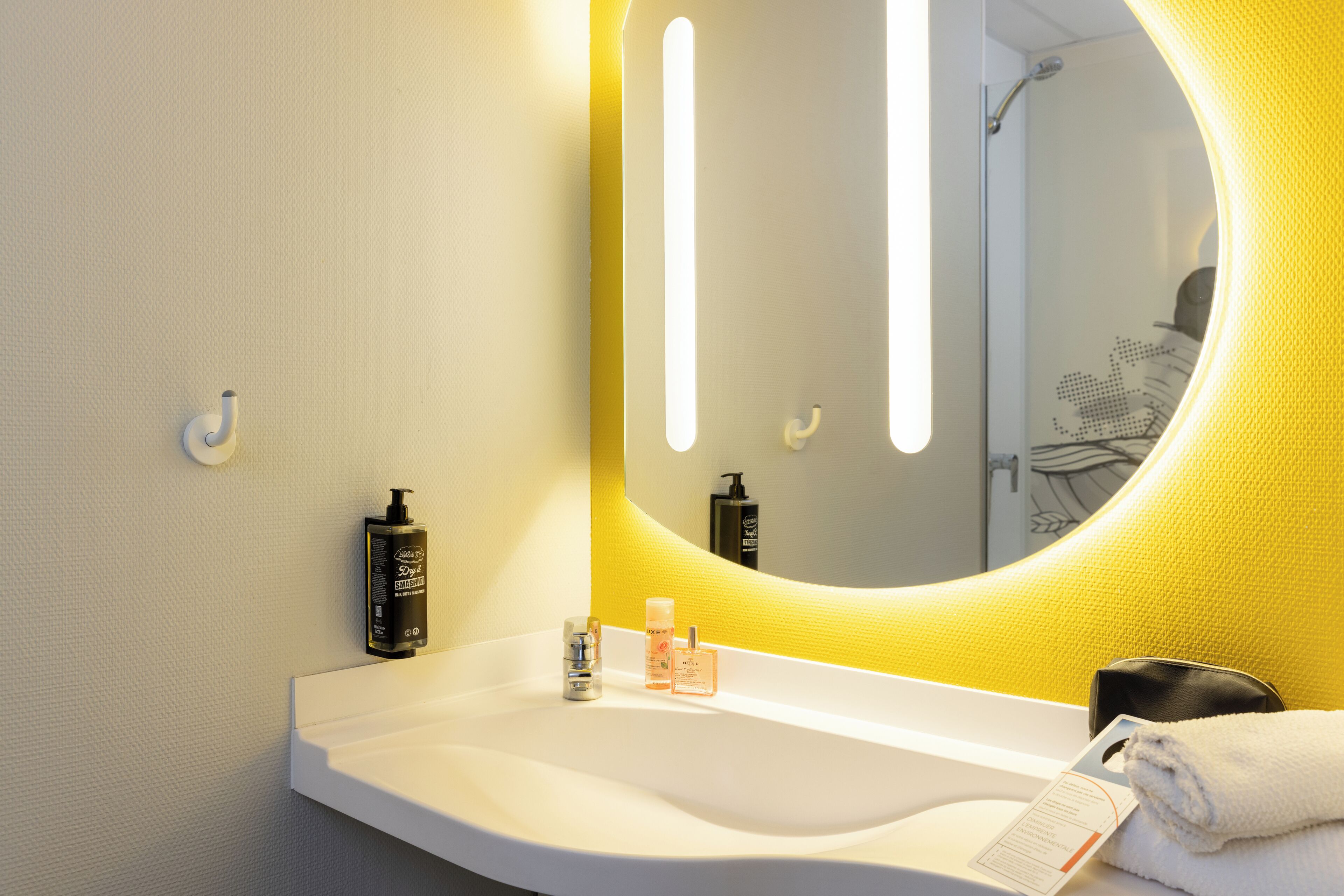 A modern bathroom with a white sink, a large mirror with a yellow accent, and toiletries on the counter.