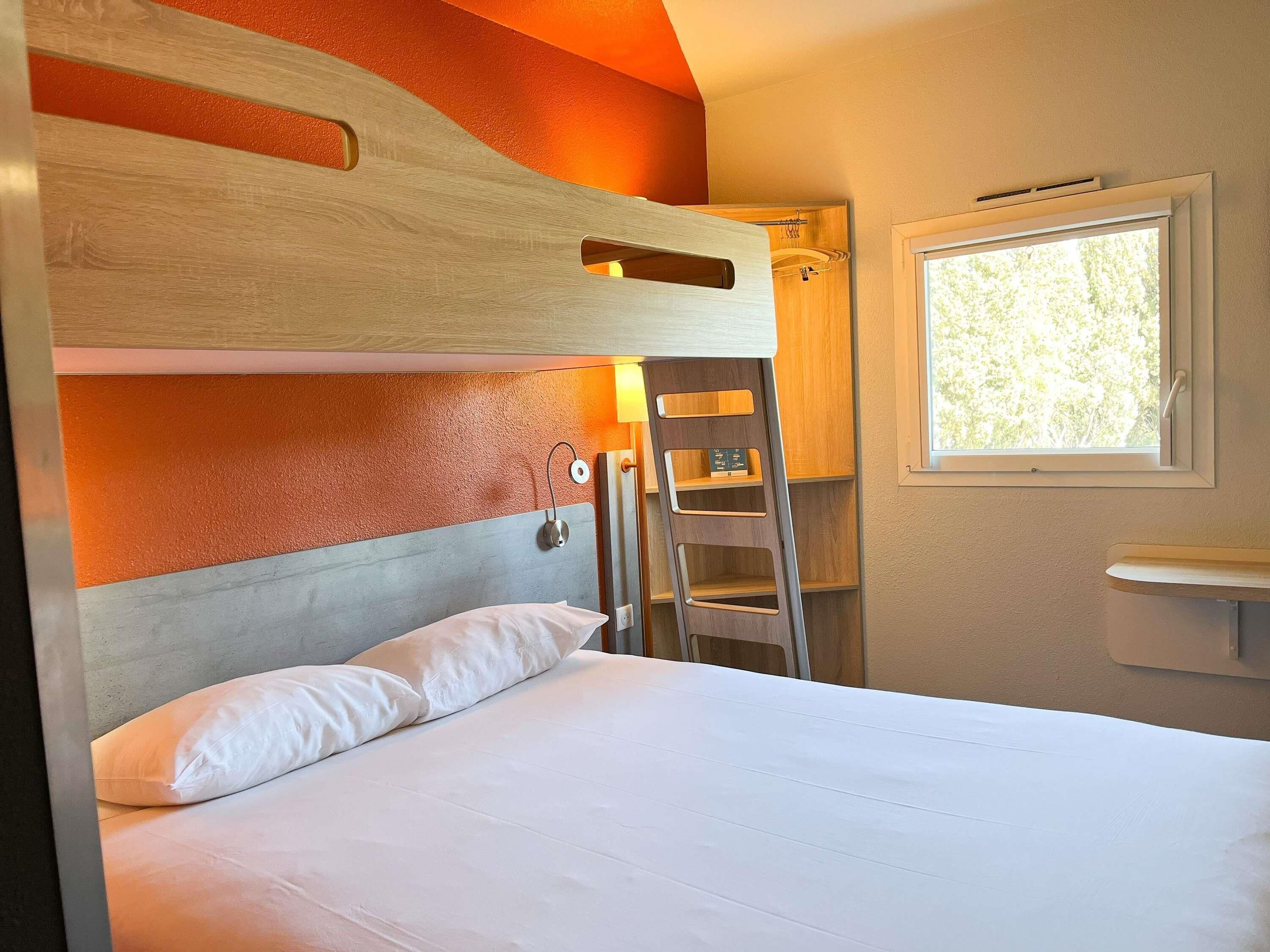 Un lit superposé avec une échelle, une table de chevet, une fenêtre avec vue et une étagère fixée au mur.