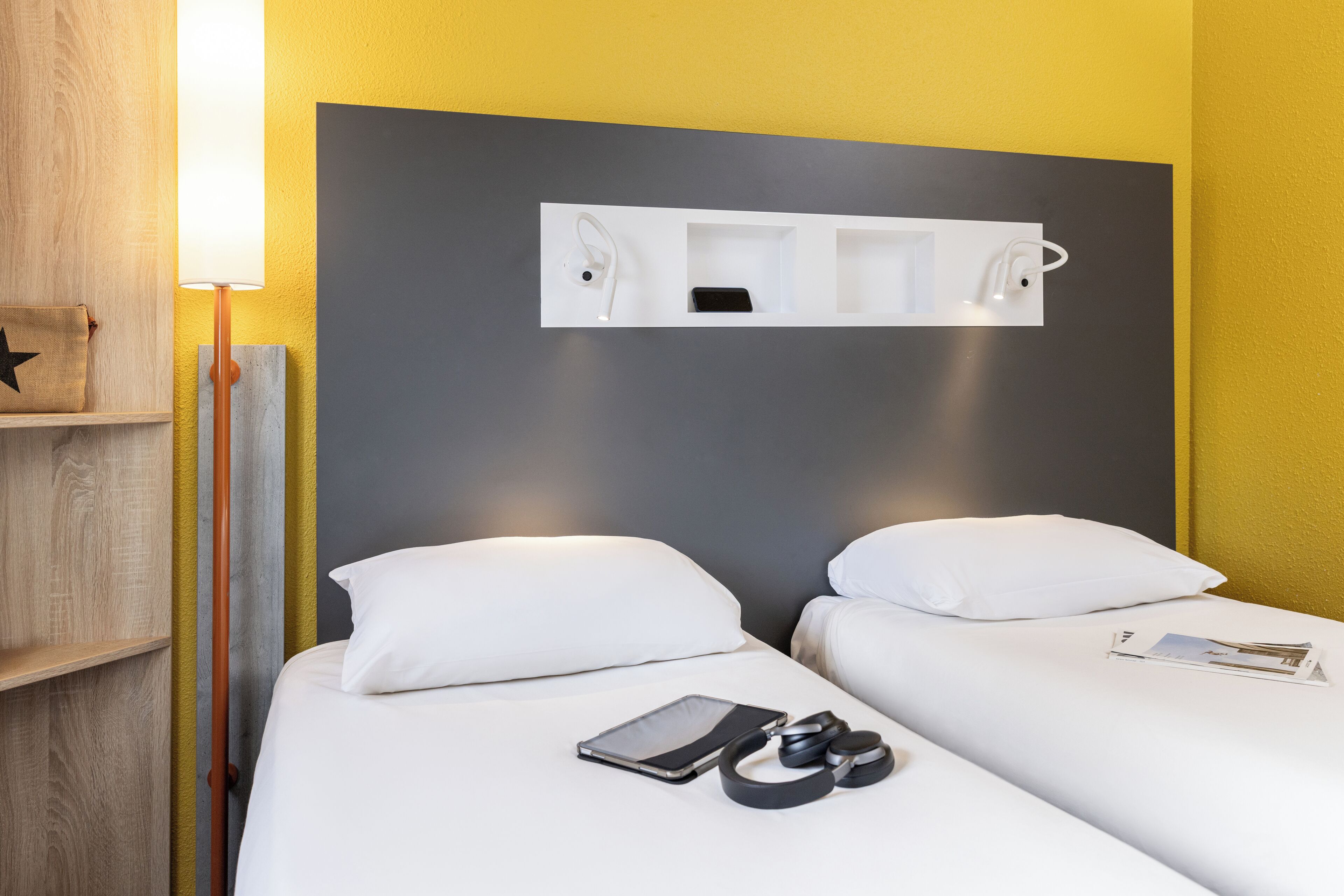 Ein Hotelzimmer mit zwei Betten, einem Nachttisch, einer Lampe, einem Regal mit Sternenverzierung und einem Wandregal mit Telefon und einem kleinen Gegenstand.