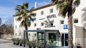 Un hôtel doté d’une entrée moderne en verre, de palmiers et surplombant un ciel dégagé.