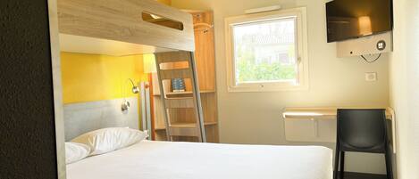 A bedroom with a bunk bed, a desk, a chair, a ladder, a TV, and a window.
