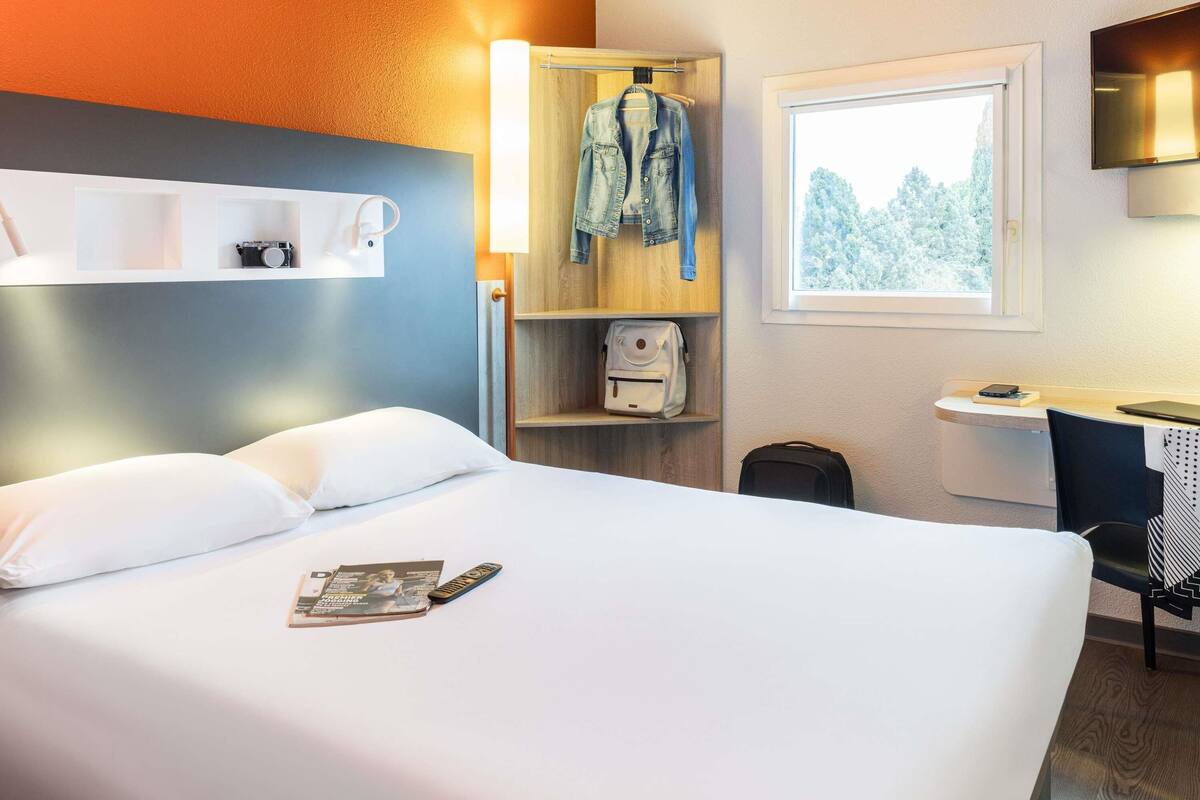 Habitación de hotel con cama, escritorio, silla, armario y ventana con vista a árboles.