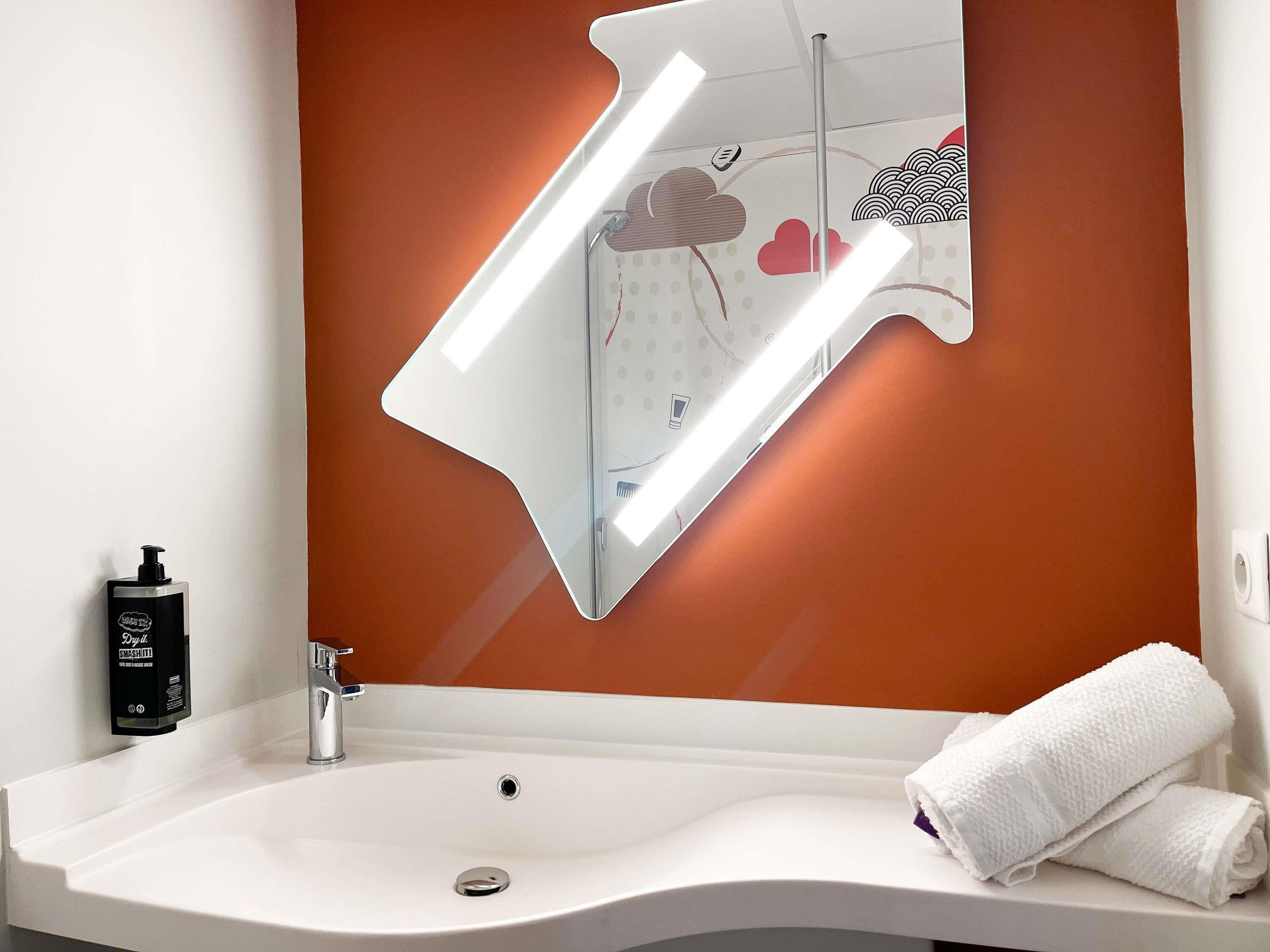 Un baño con un lavamanos blanco, un espejo con diseños de nubes y una botella de champú.