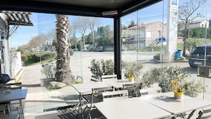 Un espace extérieur aménagé avec des tables et des chaises, un palmier, et une vue sur la rue et les bâtiments.