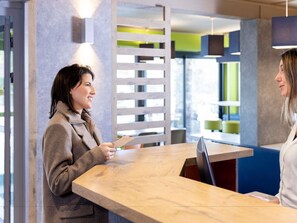 A reception desk with a wooden surface, a person holding a card, and a modern interior with a slatted wall and a blue seating area.