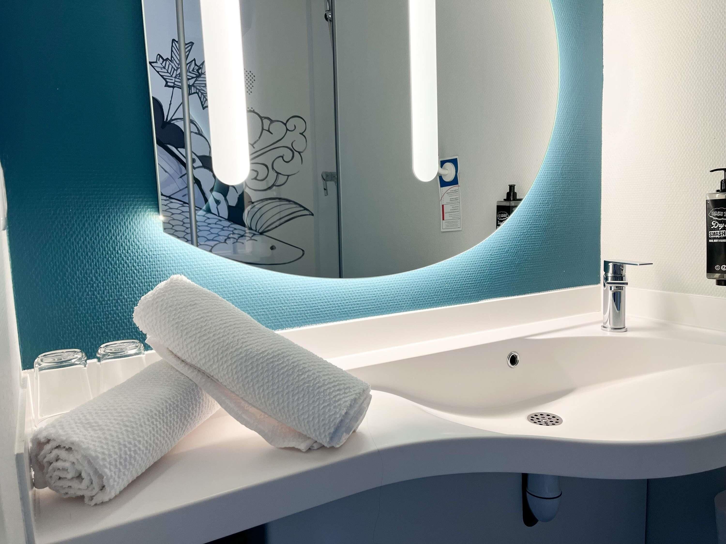 Un baño con un lavamanos blanco, una toalla y un espejo con detalles azules.