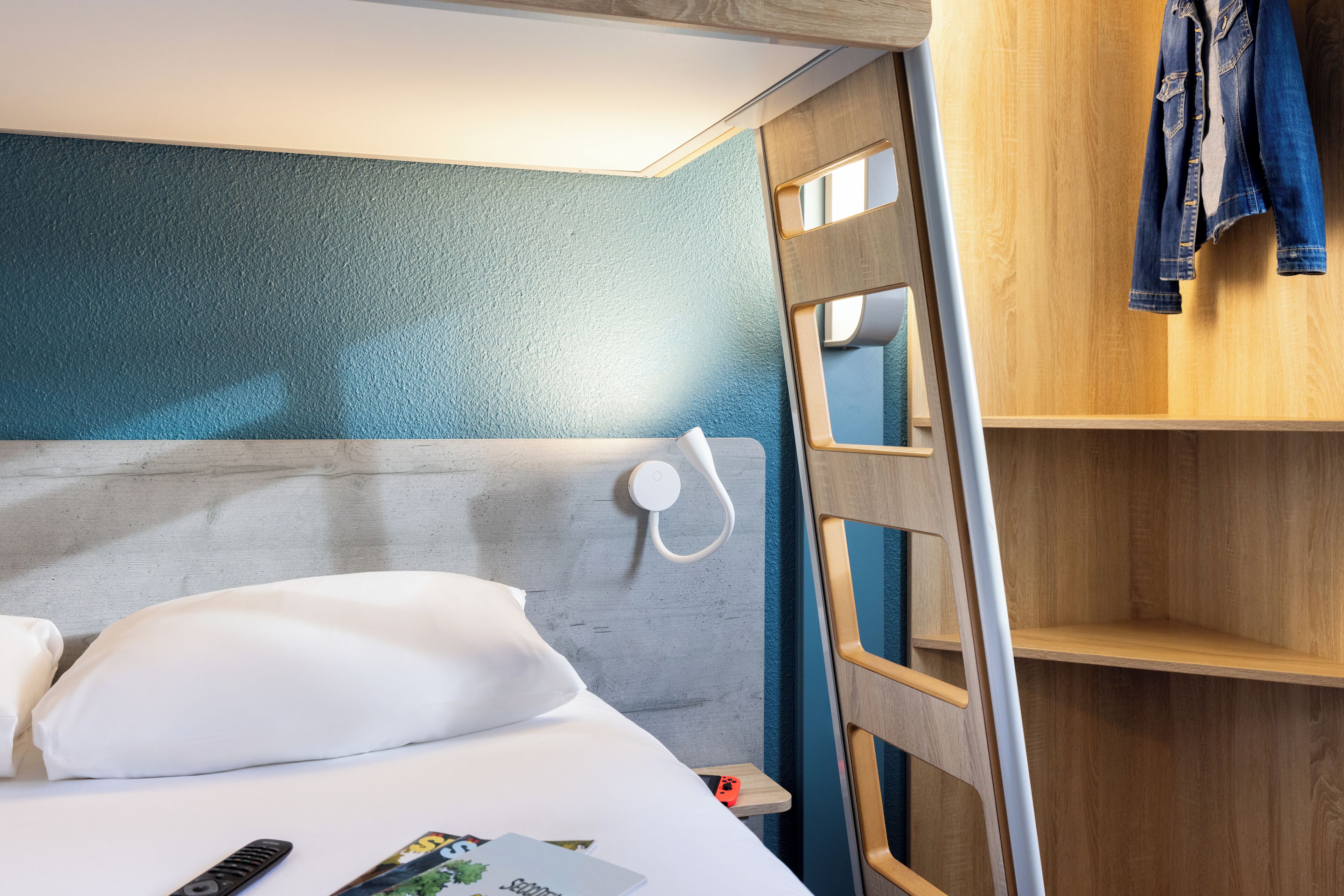 Ein Hotelzimmer mit einem Etagenbett, einer Holzleiter, einem Nachttisch und einem Kleiderschrank mit aufgehängter Kleidung.