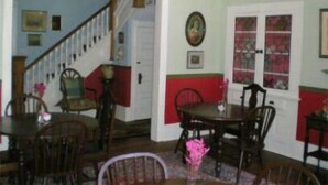 Un comedor con sillas de madera y una mesa, una araña y una escalera que sube a otra habitación.
