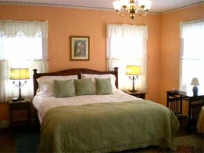 A bedroom with a bed, two bedside tables with lamps, a chandelier, and a painting on the wall.