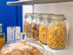 Une table où sont présentés des céréales dans des bocaux et des viennoiseries, le tout disposé sur une étagère.