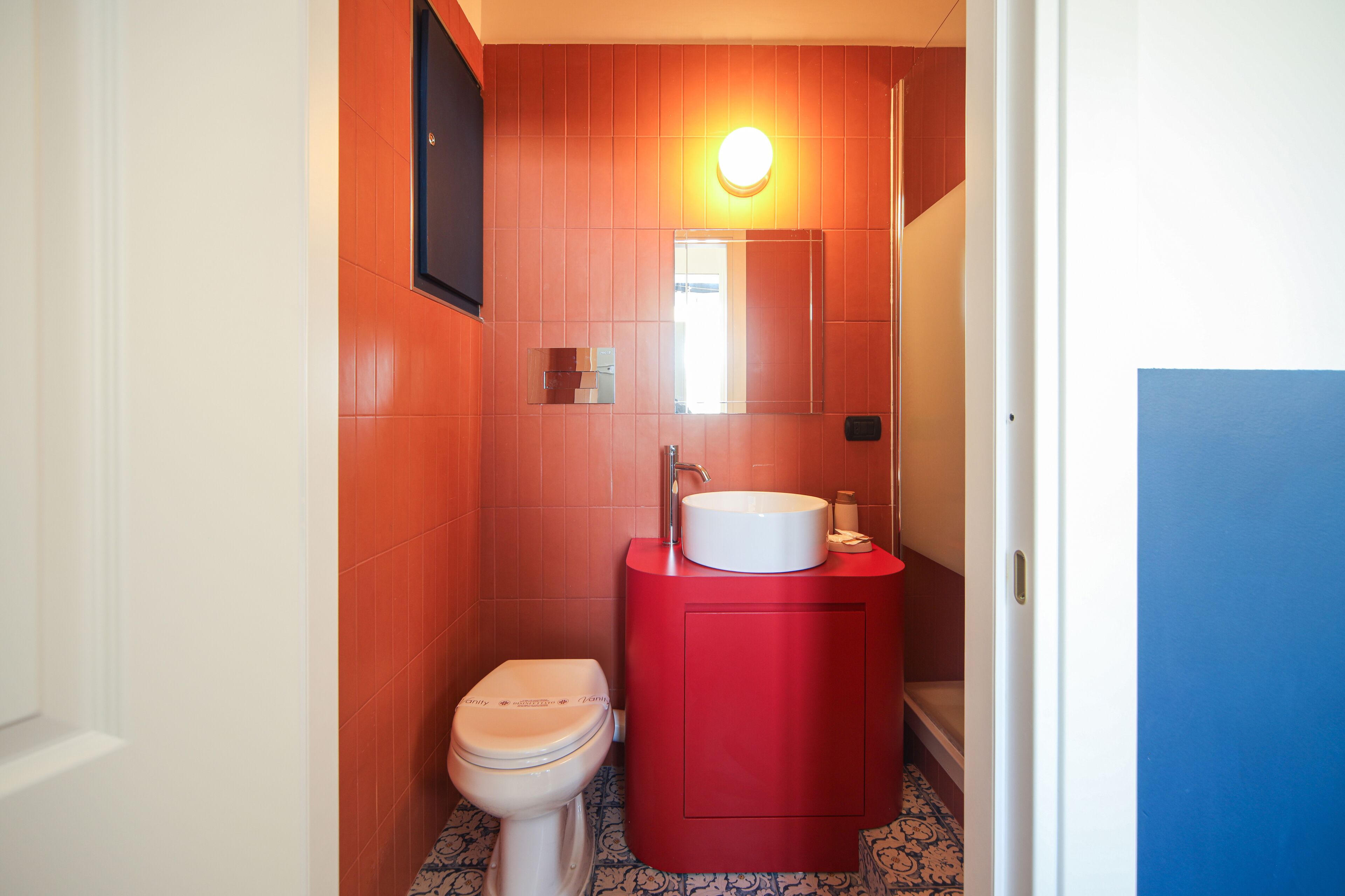 A bathroom with a red vanity, a white toilet, and a mirror above the sink.