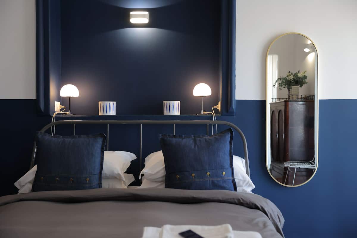 A neatly made bed with two pillows, a bedside lamp, and a mirror on the wall.