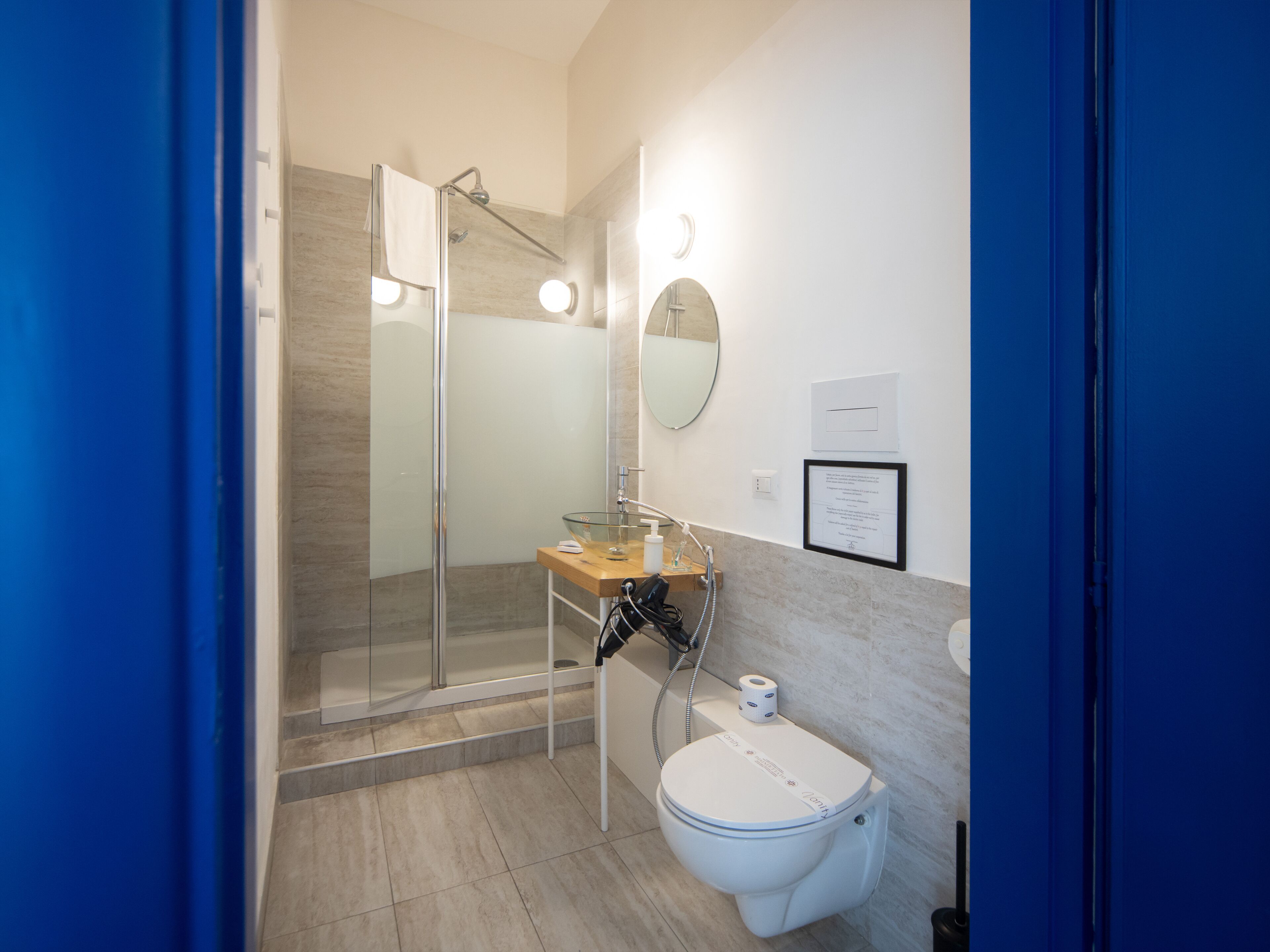 A modern bathroom with a glass shower enclosure, a wooden vanity, a toilet, and a mirror.
