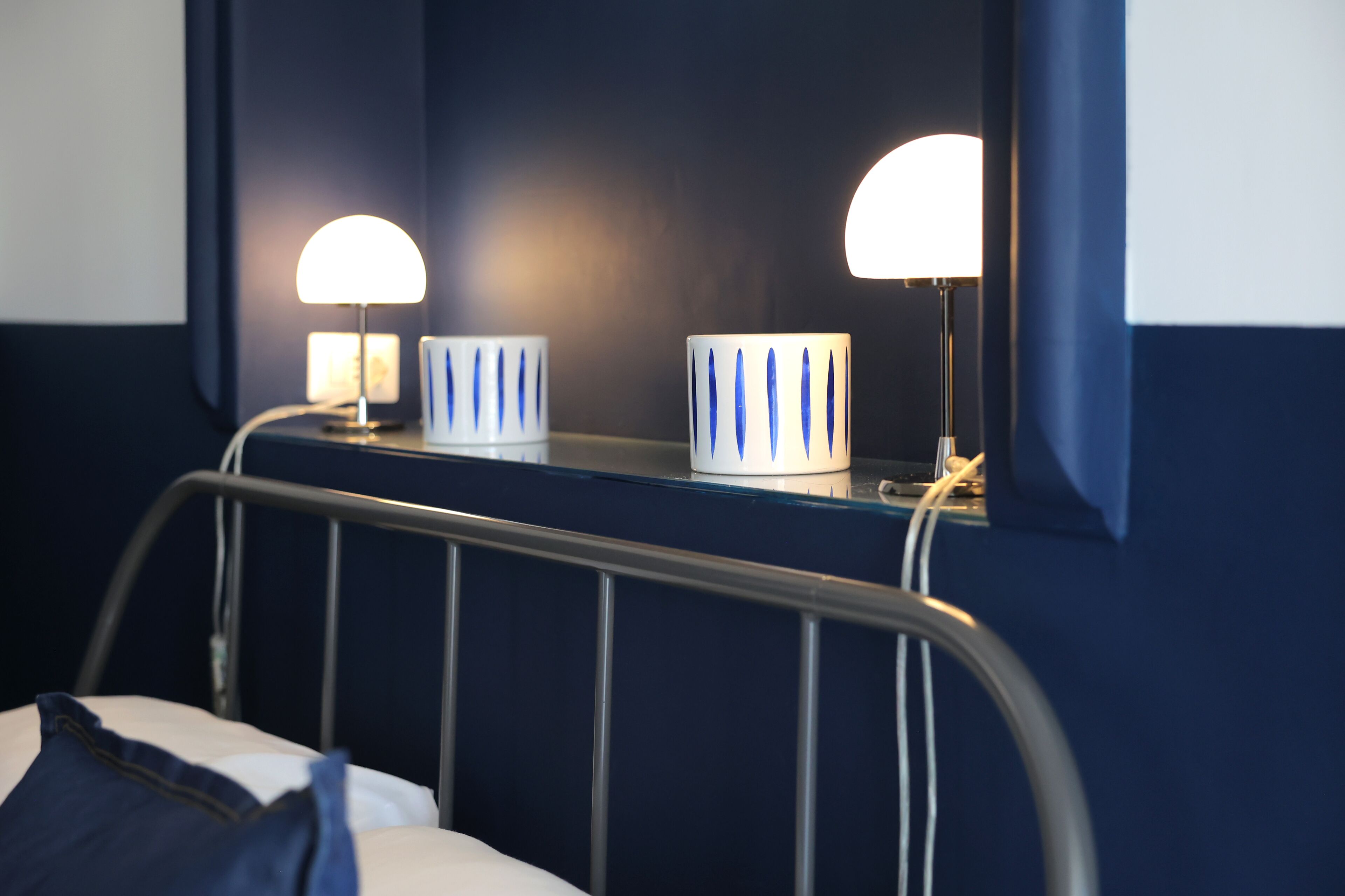 A hotel room with a bed, a bedside table with two lamps, and a window with curtains.