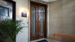 A wooden double door with glass panels, a sign above it, a potted plant, and a metal bench. - Salotto Borbonico (Naples)