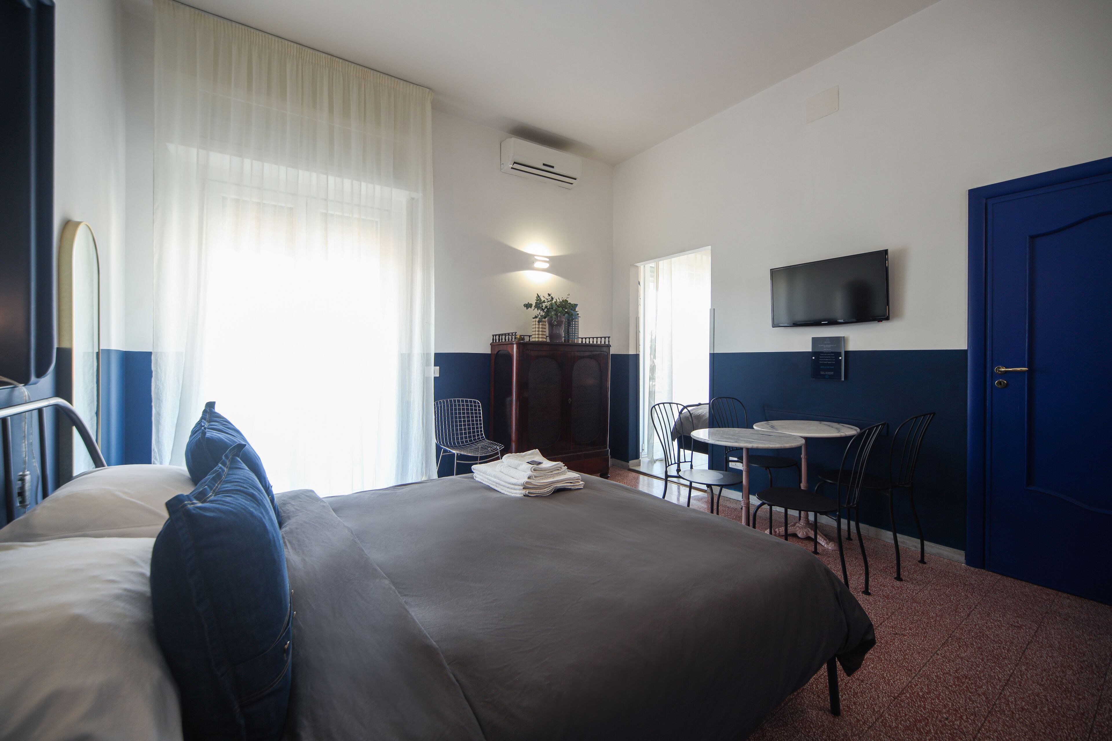 A hotel room with a large bed, a desk with chairs, a TV, and a door.