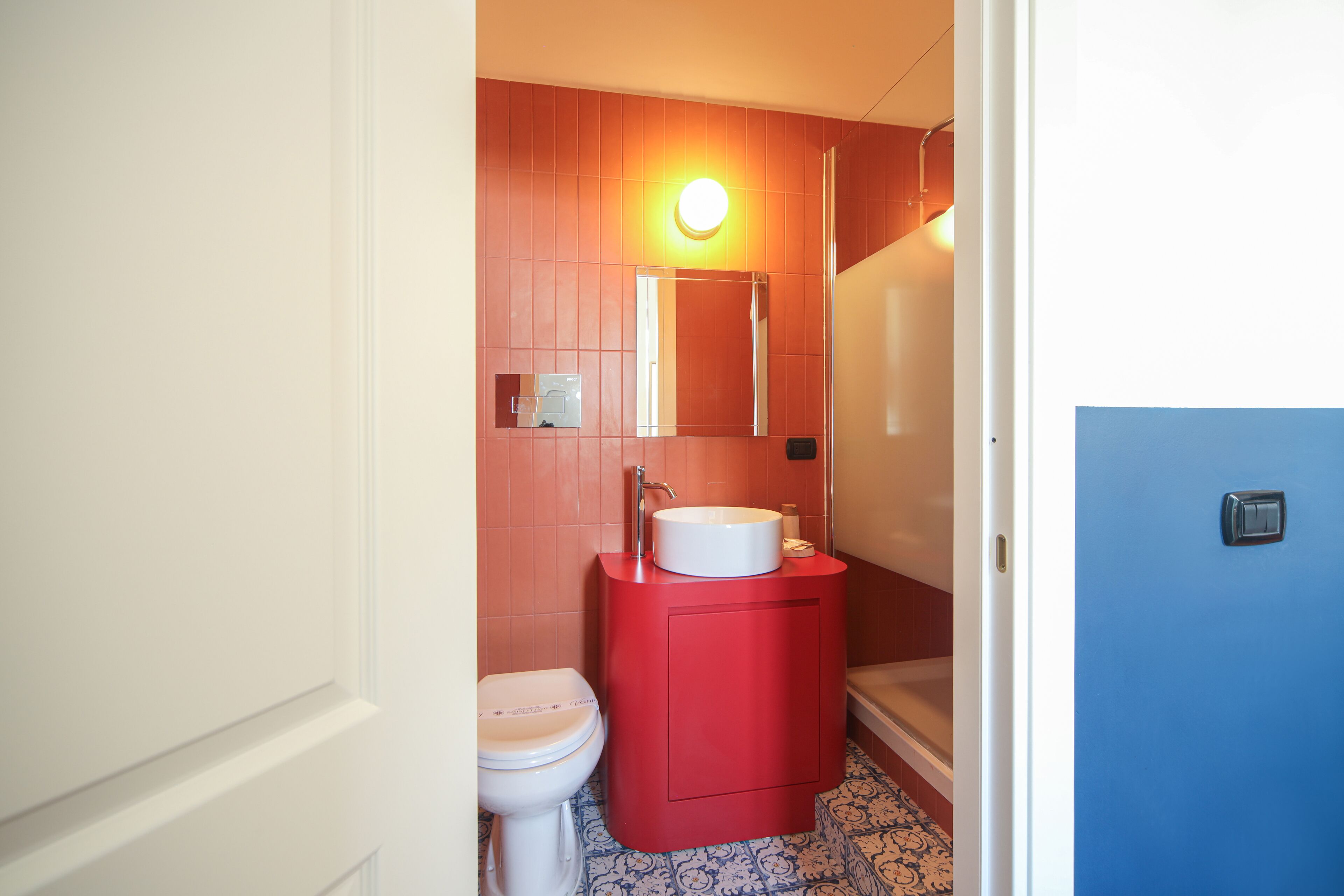 A bathroom with a white toilet, a red sink, and a blue door.