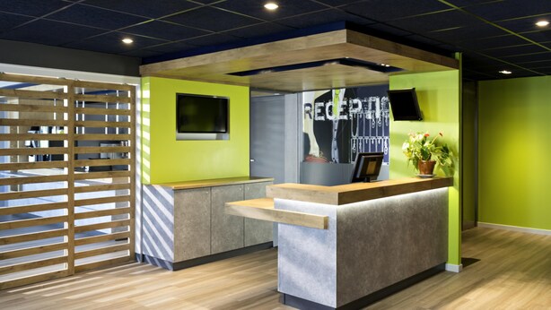 A reception desk with a modern design, a television, and a potted plant. - ibis Budget Lyon Eurexpo Chassieu (Chassieu)
