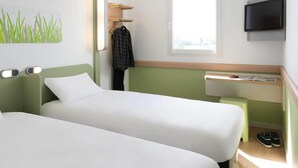 A hotel room with two beds, a TV mounted on the wall, a window, and a small table with a newspaper. - ibis Budget Lyon Eurexpo Chassieu (Chassieu)