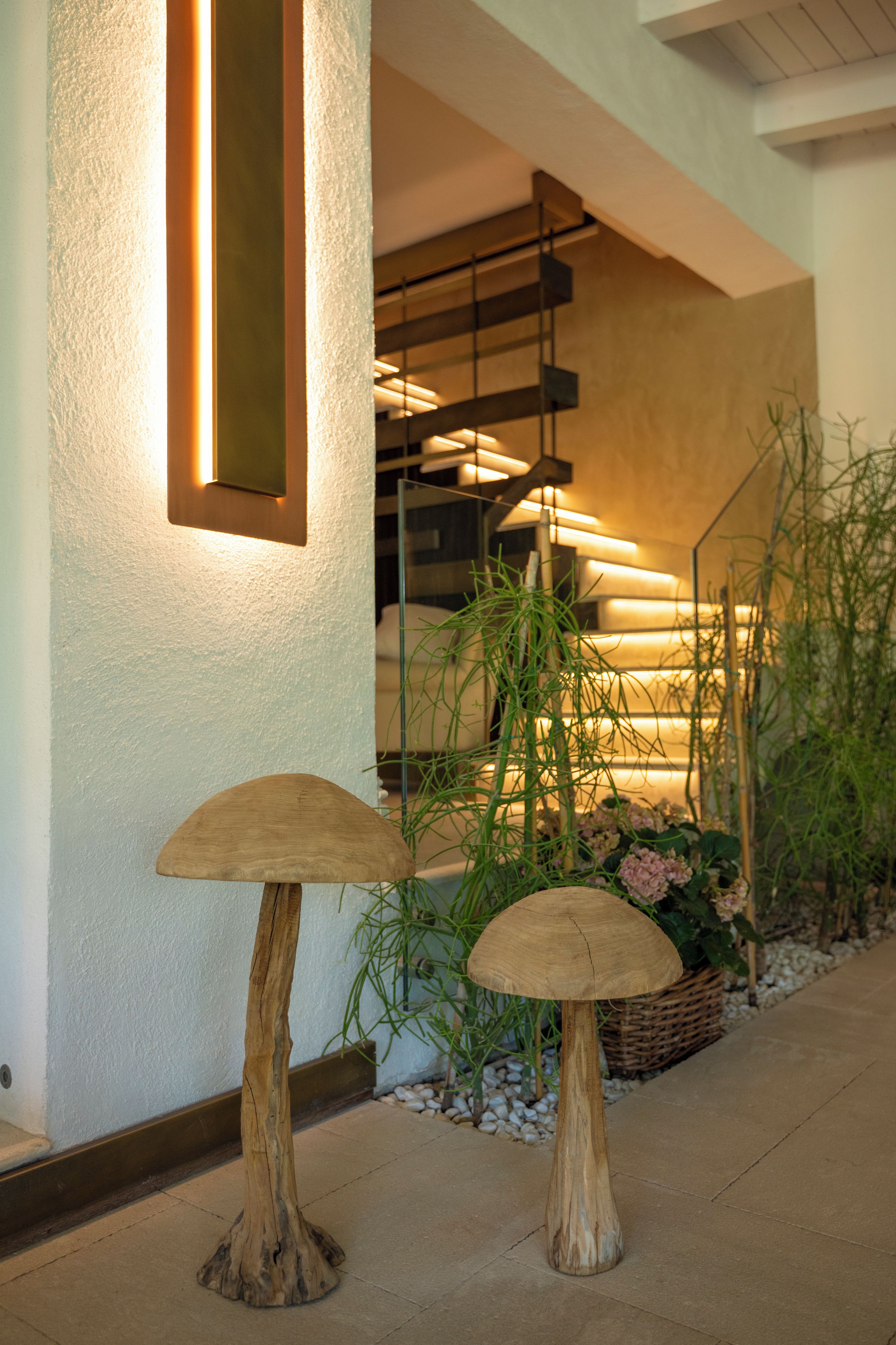 A modern interior with a staircase, wooden mushroom-shaped stools, and a plant arrangement.