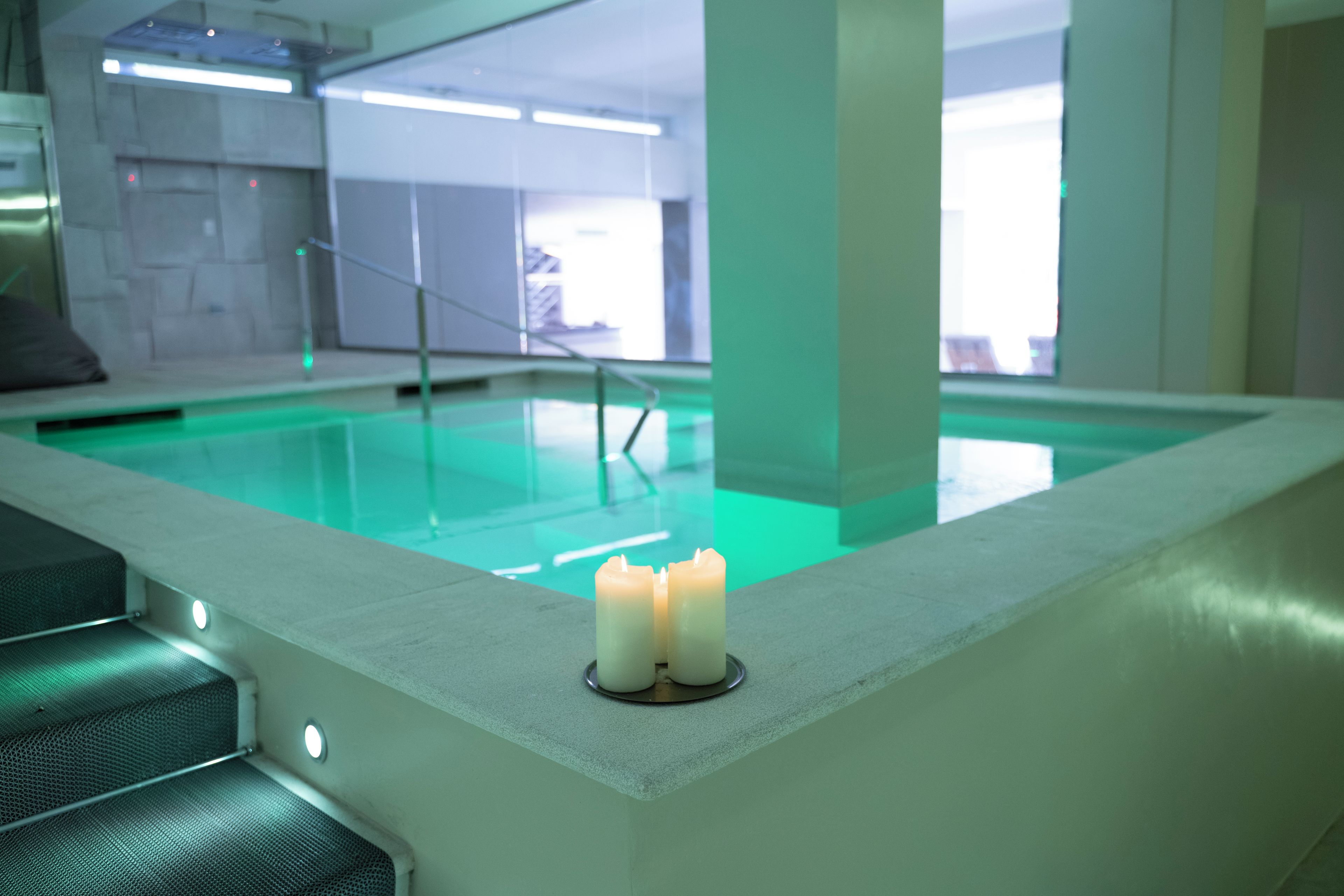 Une piscine à l’eau légèrement verdâtre, une bougie posée sur une étagère et un escalier menant vers le bas.