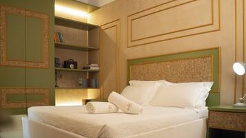 A neatly made bed with pillows and a folded towel, a bedside table with a lamp, and a bookshelf with books and a camera.