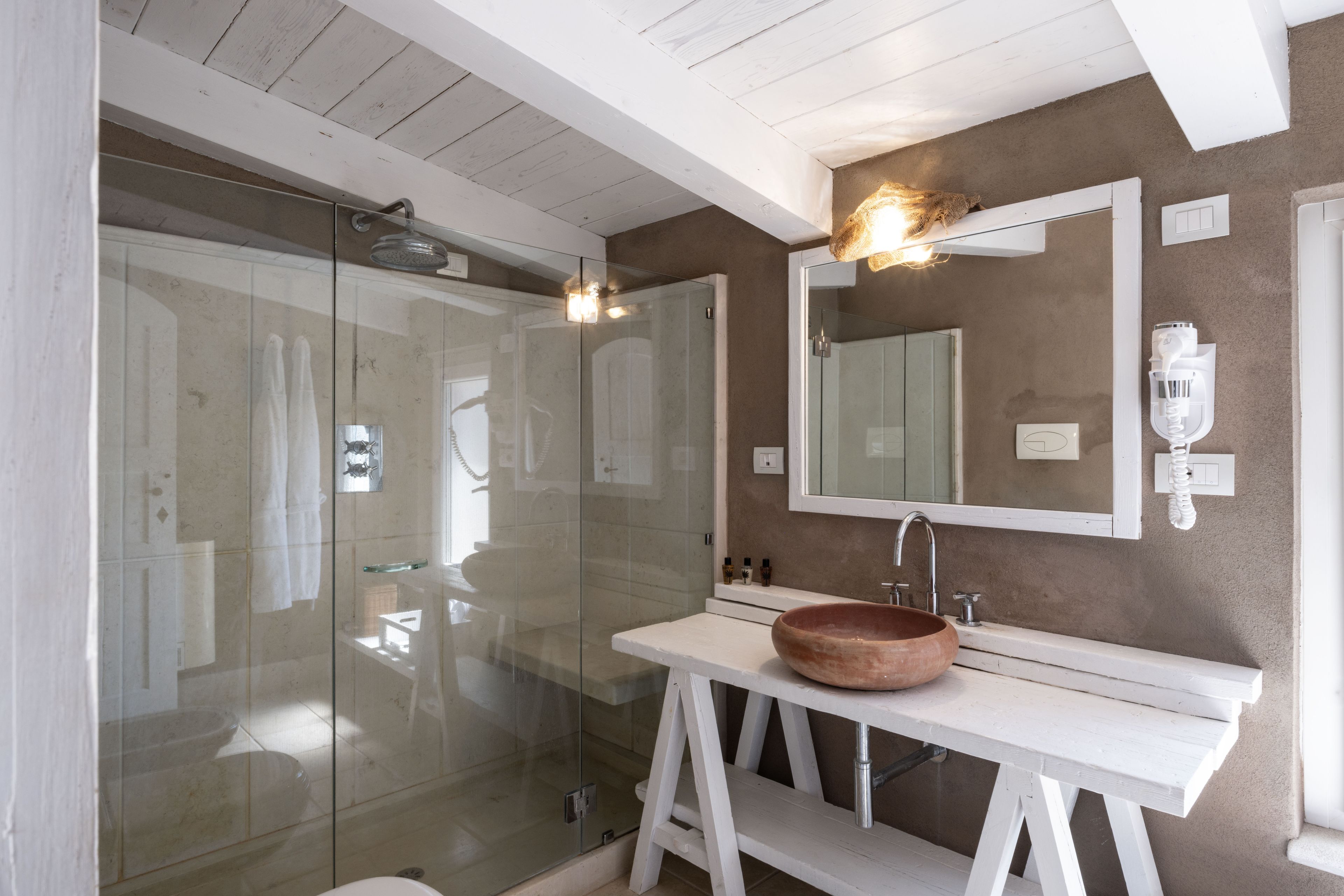 A bathroom with a glass-enclosed shower, a white vanity with a large bowl sink, and a mirror above the sink.