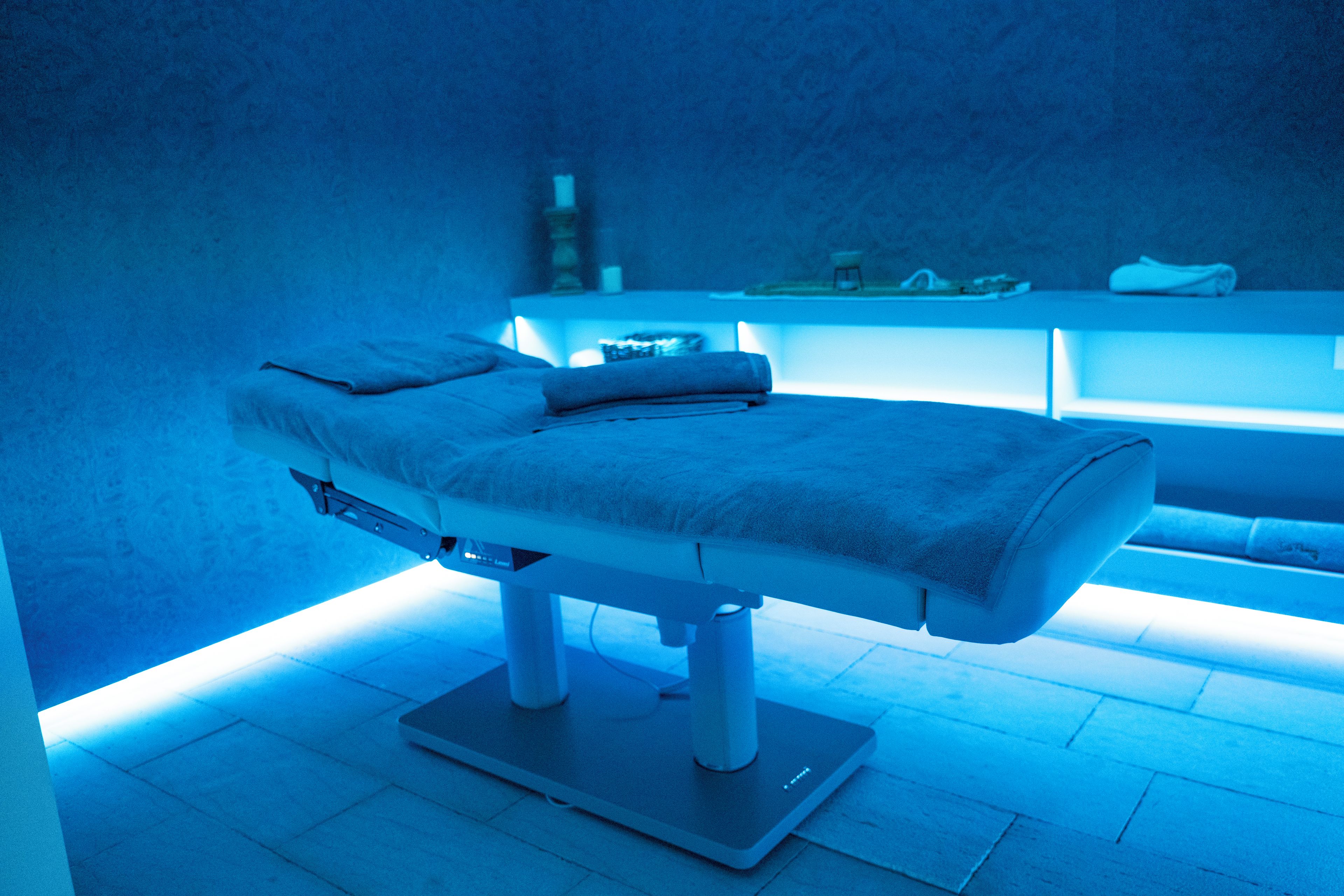 Una stanza per massaggi con un lettino da massaggio, un massaggiatore per i piedi e uno scaffale con asciugamani e altri oggetti.