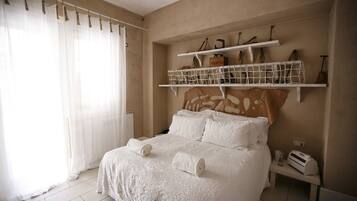 A bedroom with a bed, white curtains, a shelf with tools, and a small table.