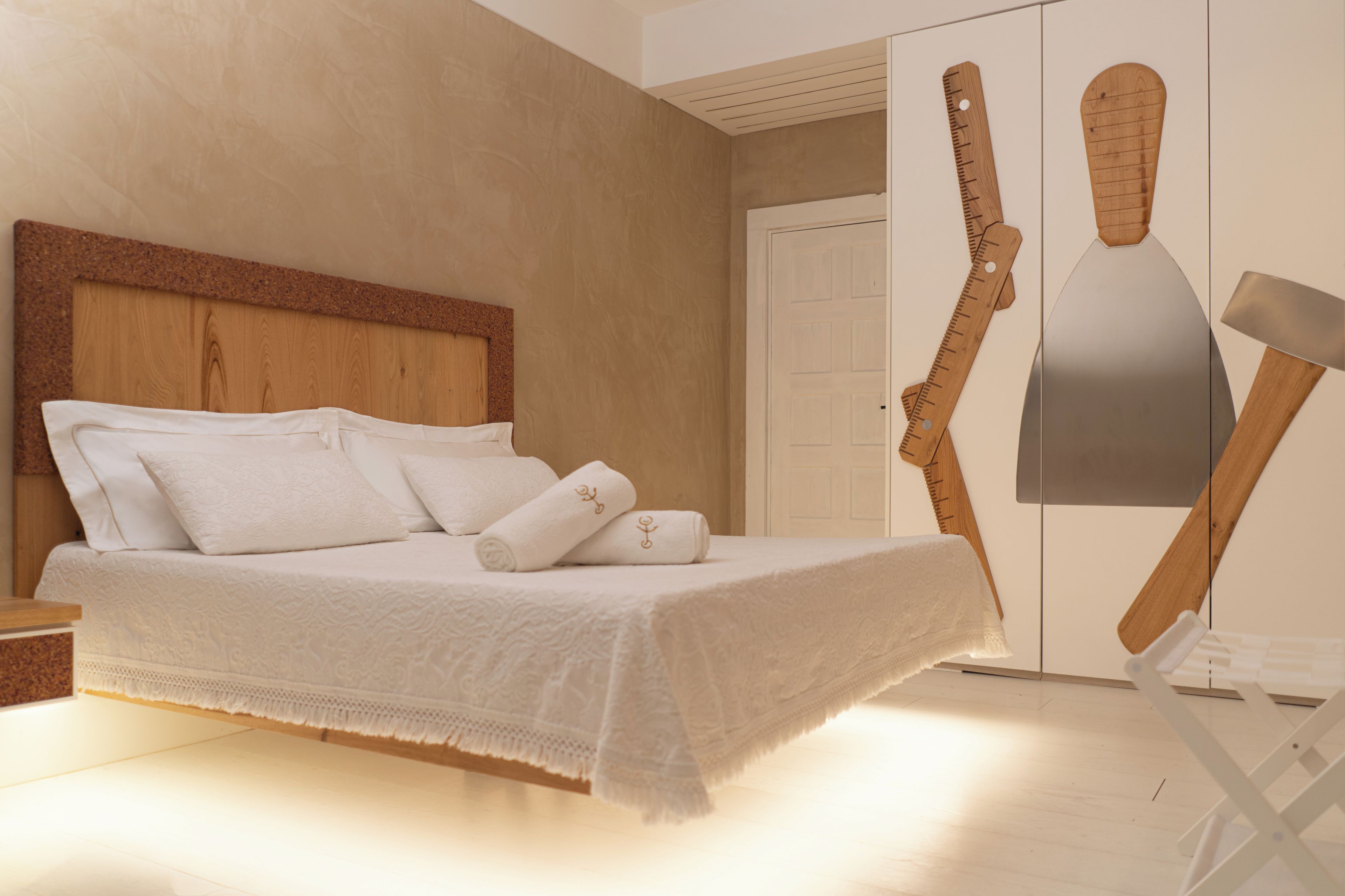 A bedroom with a wooden headboard, a bed with white linens, and a wooden door with a towel rack.