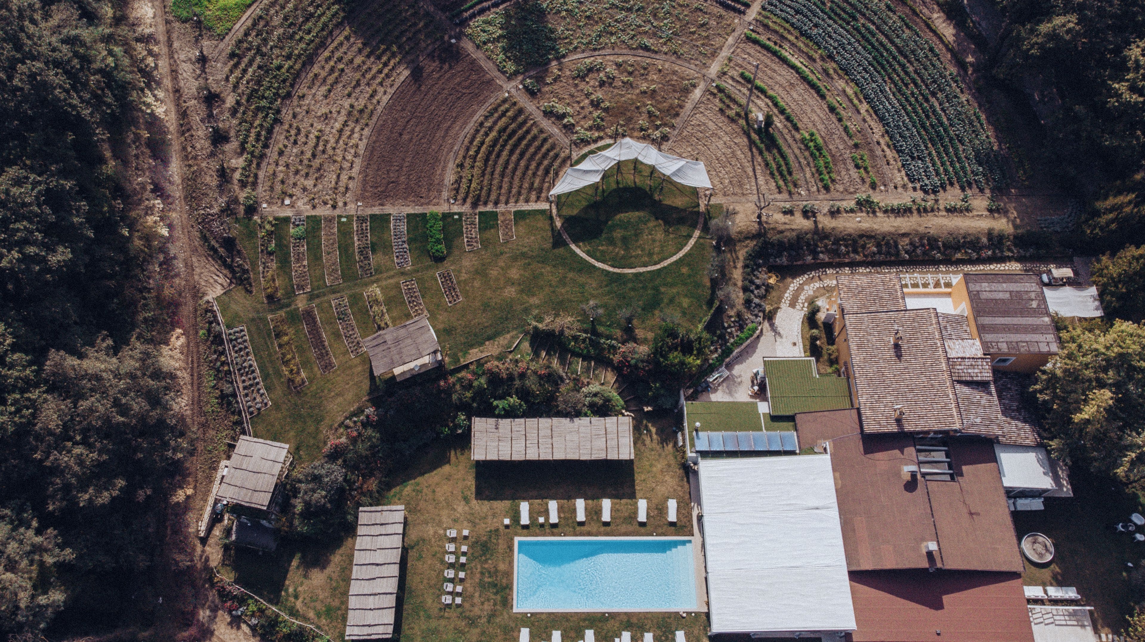 An aerial view of a property with a swimming pool, multiple buildings, and terraced gardens.