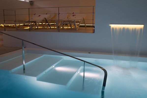 Un área de piscina interior moderna con una barrera de vidrio y una cascada.